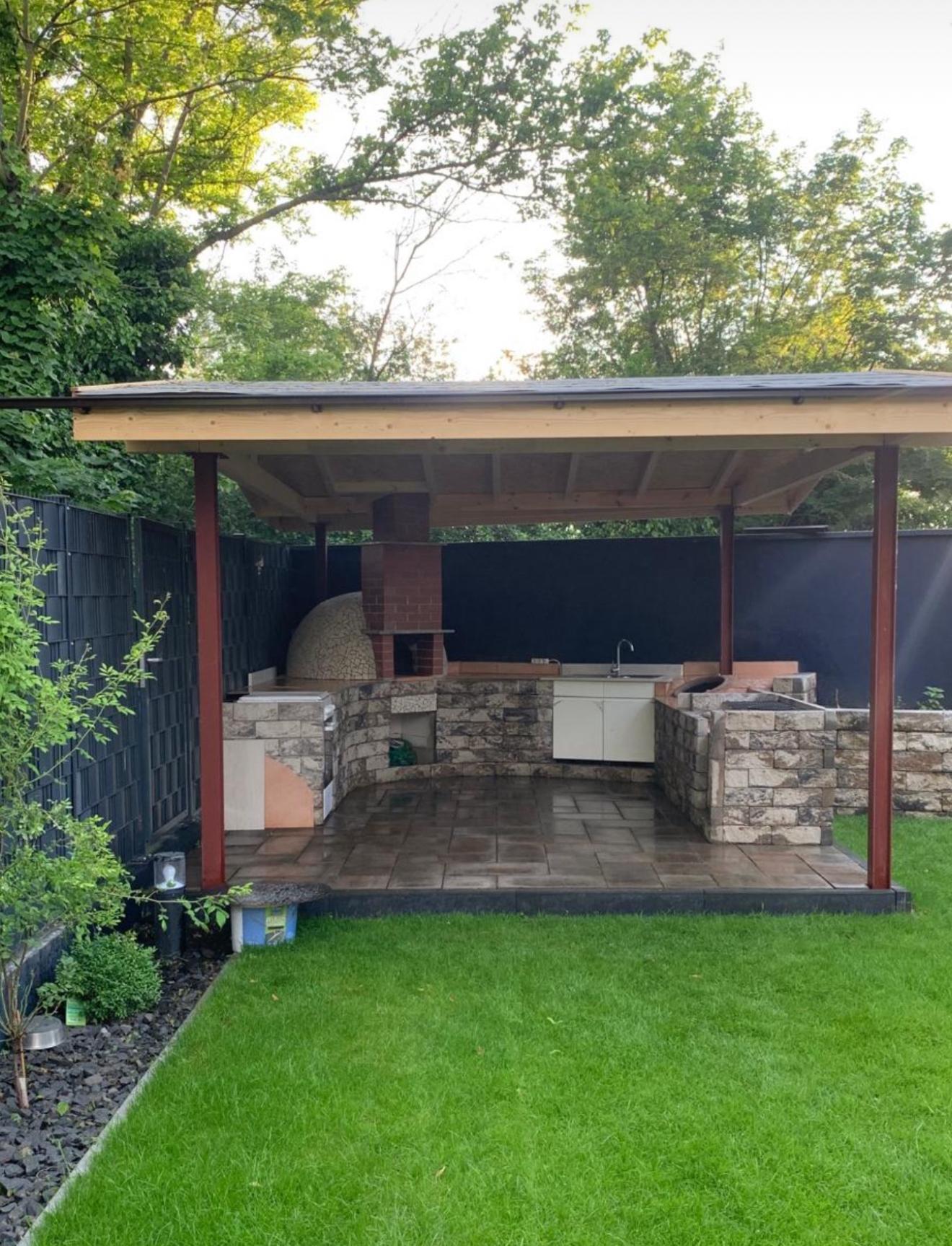 Überdachte Outdoor-Küche aus Naturstein mit Pizzaofen im Garten